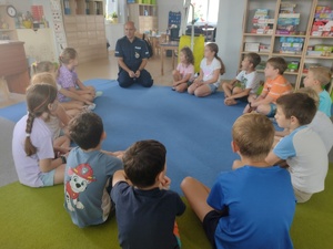 Policjant i dzieci siedzą na podłodze w kole podczas pogadanki.