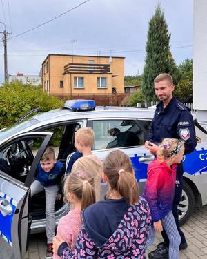 Dzieci i policjant stoją przy radiowozie.