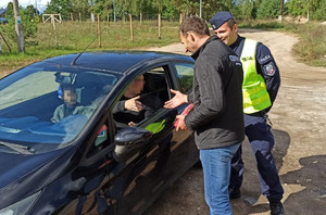 Policjant oraz Marcin Gagacki wręczają kierowcy upominki.