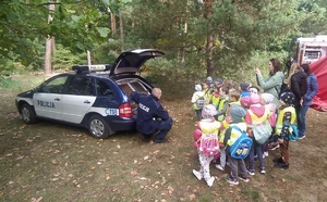 Policjant kuca przy radiowozie Obok stoją dzieci.