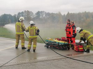 Strażacy i ratownicy medyczni przy śmigłowcu. Strażacy leją wodę