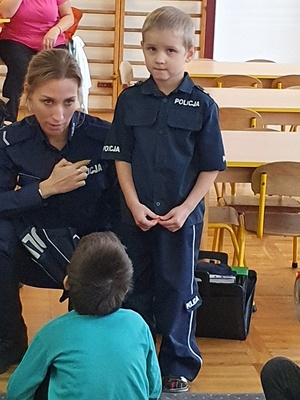 Policjantka kuca obok chłopca ubranego w strój policyjny.