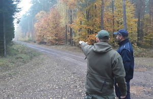 Policjant i leśnik przy drodze leśnej. Leśnik wskazuje ręką przed siebie.