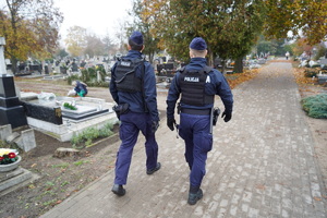 dwaj umundurowani policjanci patrolują teren cmentarza