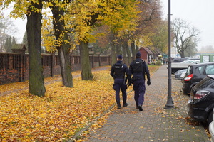 dwaj umundurowani policjanci patrolują teren cmentarza