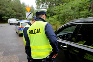 Policjant podejmujący kontrolę drogową, rozmawia z kierowcą.