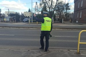 Policjant stojący na poboczu, przy jezdni podczas akcji prędkość z ręcznym miernikiem prędkości dający sygnał do zatrzymania tarczą