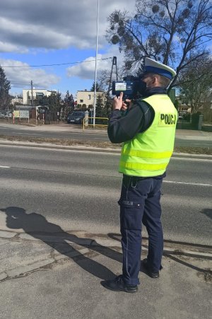 Policjant stojący na poboczu, przy jezdni podczas akcji prędkość z ręcznym miernikiem prędkości dający sygnał do zatrzymania tarczą