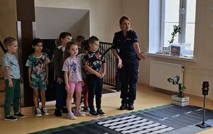 Policjantka stoi z dziećmi przed przejściem dla pieszych na macie drogowej