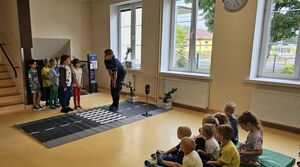 Policjantka rozmawia z dziećmi stojącymi przy macie drogowej