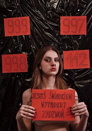 Wyróżnienie, kobieta trzyma kartkę z numerem alarmowym, wokół niej widoczne inne numery