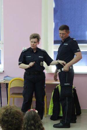 policjantka pokazuje na policjanta i kolor jego pasa służbowego