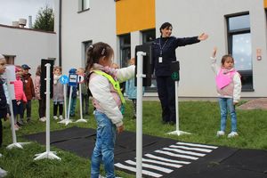 policjantka uczy dzieci żeby rozglądały się przed przejściem dla pieszych