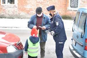 policjantka z chłopcem wręczają odblask przechodniowi