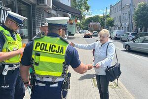 policjanci wręczają kobiecie ulotkę informacyjną
