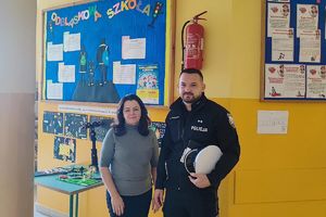 policjant z nauczycielką przy szkolnej tablicy z informacjami do konkursu i gazetką informacyjną