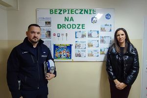 policjant z nauczycielką przy szkolnej tablicy z informacjami do konkursu i gazetką informacyjną
