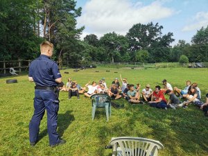 policjant prowadzi prelekcję dla dzieci siedzących na trawie