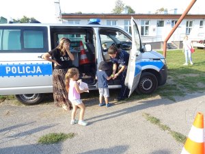 stojąc przy radiowozie policjantka rozdaje dzieciom odblaskowe opaski