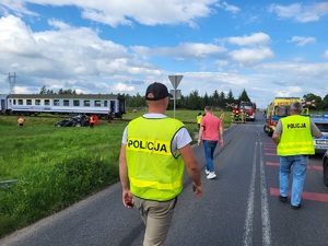 policjanci idą w strone miejsca wypadku, w tle widać pociąg oraz uszkodzony samochód