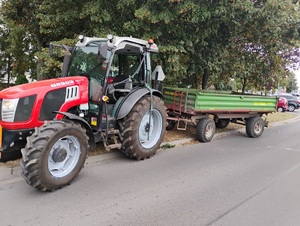 ciągnik z przyczepą stojący częściowo na jezdni, a cześciowo na pasie zieleni