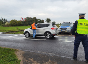 pracownik kolei wręcza ulotkę kierowcy samochodu przy przejeżdzie kolejowym