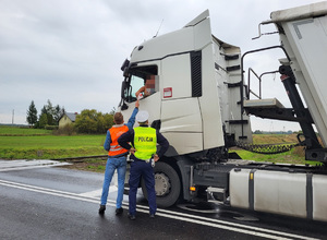 pracownik kolei z policjantem wręcza ulotkę kierowcy samochodu przy przejeżdzie kolejowym