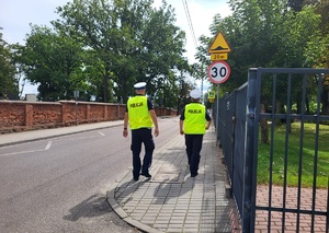 dwóch policjantów idzie chodnikiem w kierunku przejściadla pieszych
