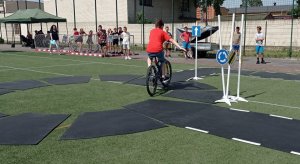 Uczeń zdaje egzamin praktyczny na kartę rowerową. Chłopiec jadący na rowerze pokazuje jak poruszać się właściwe na skrzyżowaniu.