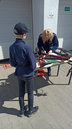 Policjantka znakuje rower. Przed  nią stoi chłopiec. Rower położony jest na stole.