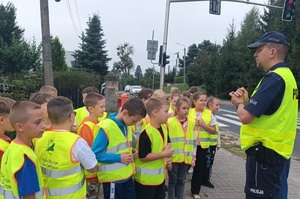 Dzielnicowy stoi razem z uczniami przed przejściem dla pieszych