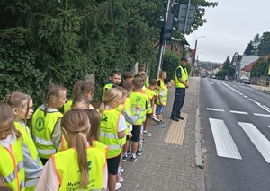 Dzielnicowy z uczniami stoi przed przejściem dla pieszych