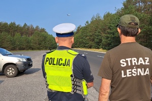 Policjant i Strażnik Leśny obserwują drogę i przelatujący samolot