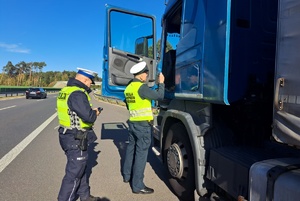 Inspektor podaje dokumenty kierowcy ciężarówki, policjant stoi obok
