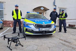 Policjanci stoją przy radiowozie, z przodu prezentują drona