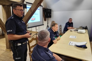 Mundurowi siedzą przy stoliku, jeden z nich stoi, prowadzi rozmowę