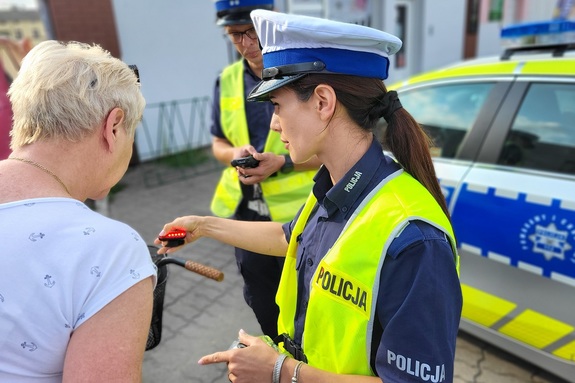 Policjantka pokazuje kobiecie sposób działania lampki rowerowej