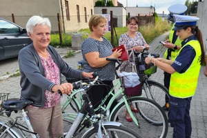 Policjantka trzyma w ręku lampki rowerowe, rowerzystki słuchają rad policjantów