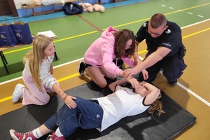 Policjanci prowadzący spotkanie z młodzieżą na sali gimnastycznej szkoły podstawowej, na zdjęciach dzieci z hulajnogami i kaskami ochronnymi