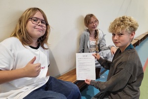 Policjanci prowadzący spotkanie z młodzieżą na sali gimnastycznej szkoły podstawowej, na zdjęciach dzieci z hulajnogami i kaskami ochronnymi