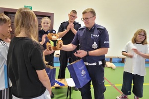 Policjanci prowadzący spotkanie z młodzieżą na sali gimnastycznej szkoły podstawowej, na zdjęciach dzieci z hulajnogami i kaskami ochronnymi