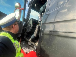 Policjant ruchu drogowego stoi przy kabinie pojazdu ciężarowego, który kontroluje.