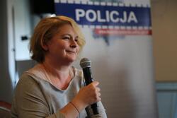 Dominika Ostałowska z mikrofonem, na tle baneru z napisem "Policja"